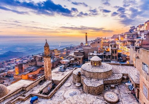 Gün batımında Mardin eski şehri: minareler, kubbeler ve Mezopotamya ovasının üstünde taş çatılar.